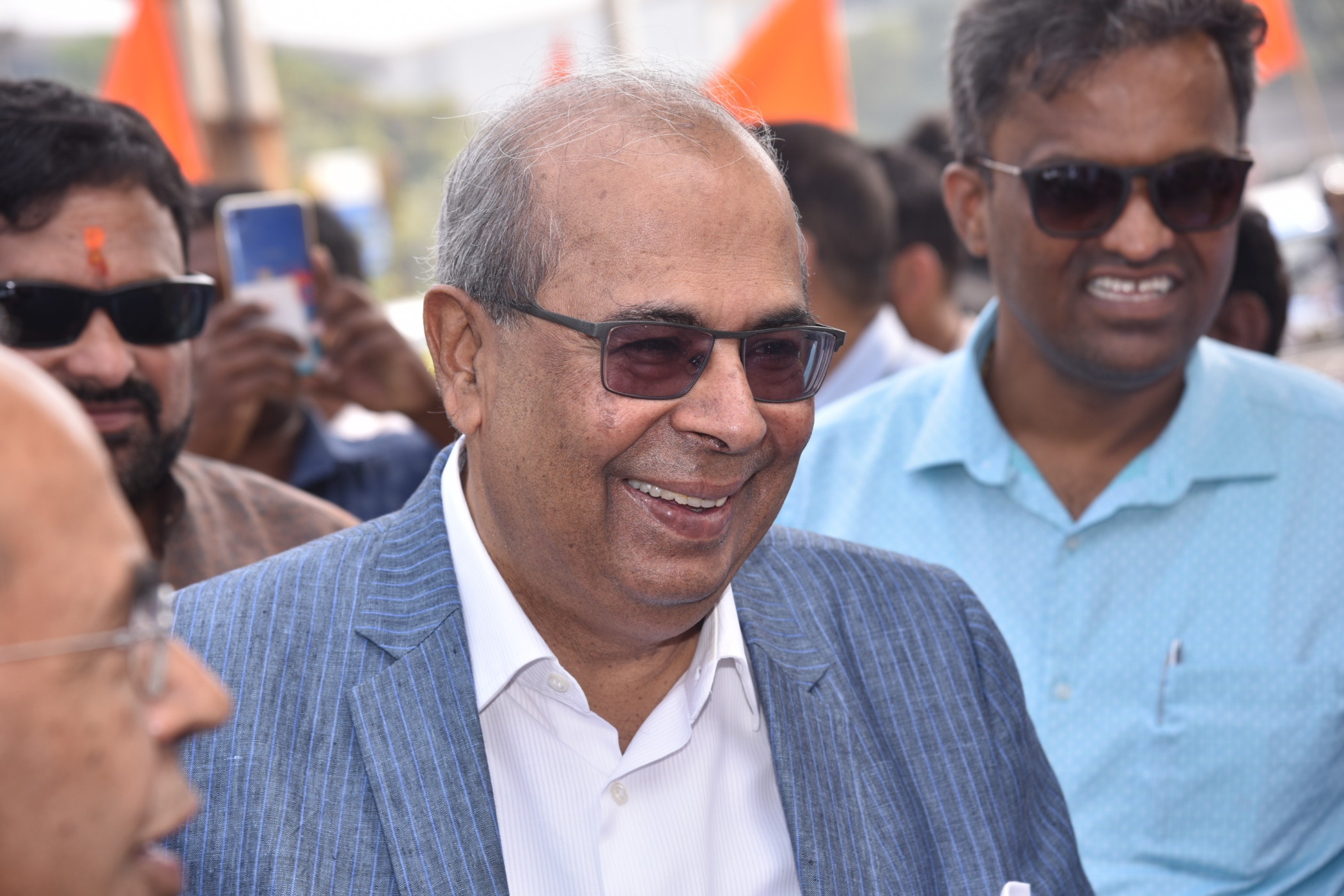 Prakash Hinduja smiling~ Wearing black sunglasses and light blue suit with white shirt.